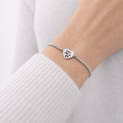 Pulseira prateada com pendente em forma de coração com texto gravado