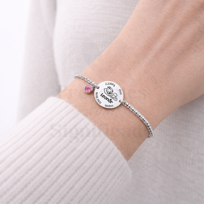 Pulseira prateada com pendente redondo personalizado com dados de bebé e pendente pequeno rosa no pulso