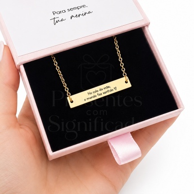 Colar dourado numa caixa de joia rosa com interior preto e texto gravado