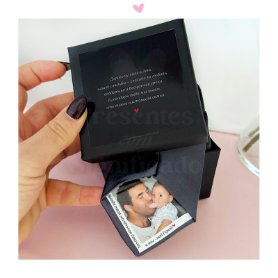 Caixa preta com placa branca e imagem de homem e bebé, com texto em russo na tampa