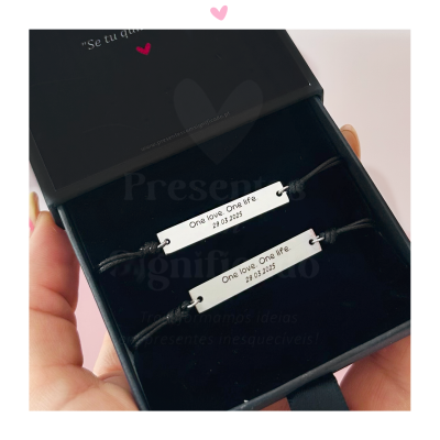 Par de pulseiras de corda preta com placas metálicas gravadas em caixa preta