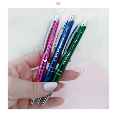 Três canetas metálicas coloridas em mão sobre fundo branco e rosa