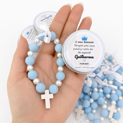 Pulseira azul com cruz branca e caixa redonda com texto de batizado