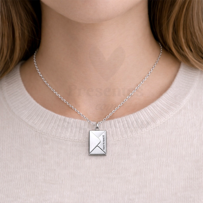 Colar prateado com pendente em forma de envelope e gravação Adoro-te Mami numa camisola bege clara