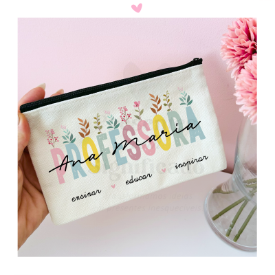 Bolsa de tecido branca estampada com palavra PROFESSORA e flores, segurada por mão, com vaso de flores ao lado