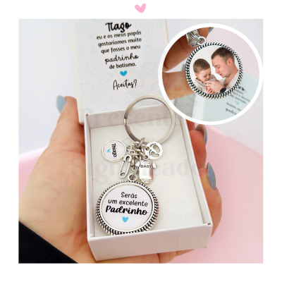 Porta-chaves com medalhão e pendentes dentro de caixa branca com texto em português