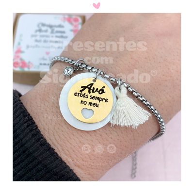 Pulseira prateada com medalhas dourada e branca e tassel branco no pulso