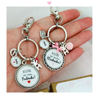 Dois porta-chaves prateados com pendentes personalizados e figuras decorativas na mão.