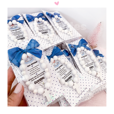 Pulseiras brancas com crucifixo e laços azuis em embalagens com texto e nome GUSTAVO