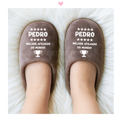 Chinelos castanhos com texto branco Pedro melhor afilhado do mundo sobre superfície peluda branca