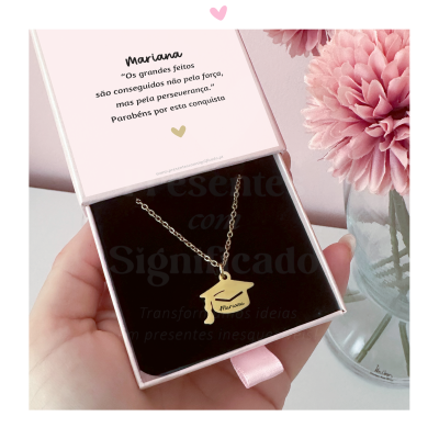 Colar prateado com pendente de capelo em caixa cor-de-rosa aberta junto a vaso com flor rosa