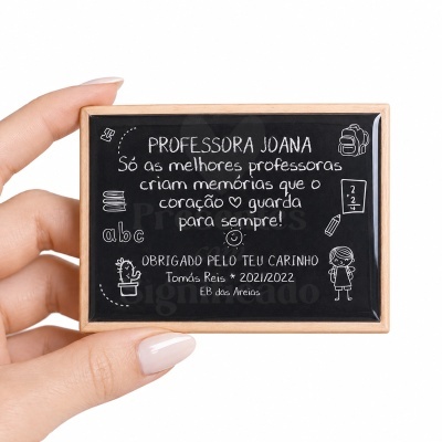 Quadro pequeno com moldura de madeira clara e texto branco dedicado a professora Joana