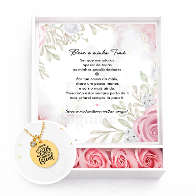 Caixa branca com cartão floral, colar dourado com pendente redondo e rosas artificiais cor-de-rosa