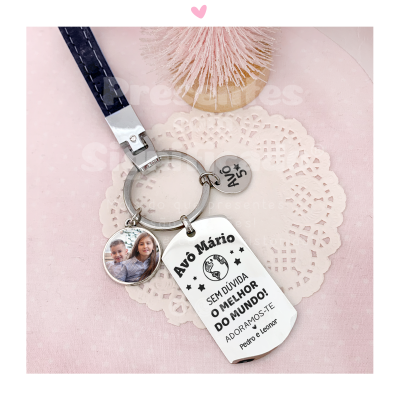 Chaveiro prateado com chapa retangular, medalhão com fotografia de crianças e coração com texto, sobre guardanapo decorativo branco e base rosa