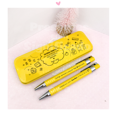 Estojo amarelo com frases e desenhos infantis e duas canetas amarelas sobre superfície rosa
