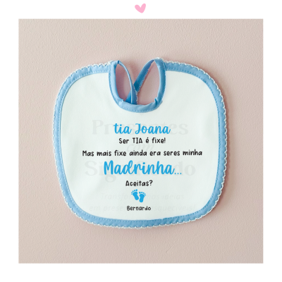 Babete branco com bordas azuis e texto para madrinha pendurado numa parede rosa