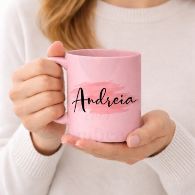 Caneca rosa com o nome Andreia em letras pretas e fundo rosa, segurada por duas mãos.