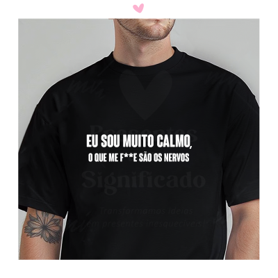 Homem com t-shirt preta com texto branco e tatuagem de flor no braço, fundo cinzento claro.