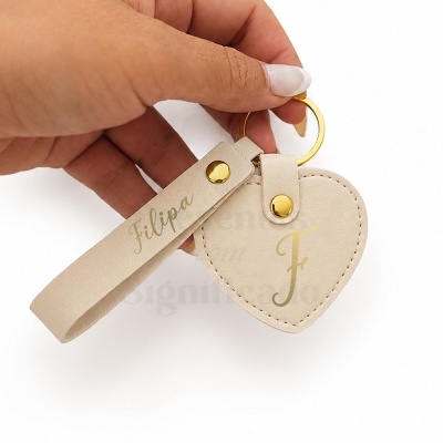 Porta-chaves em forma de coração bege com gravação dourada e argola dourada.