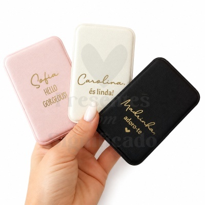 Power banks rosa, branca e preta com texto dourado segurados por uma mão