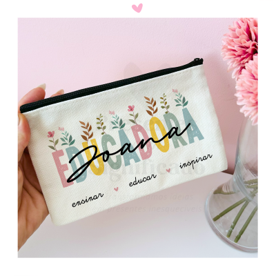 Necessaire branca com texto colorido e preto, perto de flores cor-de-rosa num vaso transparente