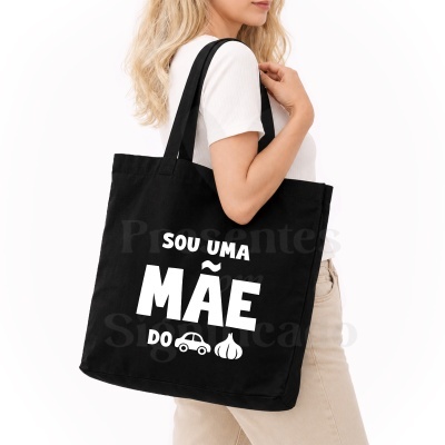 Mala tote preta com texto branco e imagens ao ombro de uma mulher de perfil