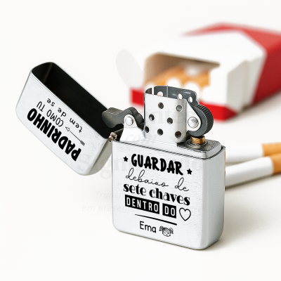 Isqueiro metálico prateado aberto com texto em português e caixa de cigarros ao fundo