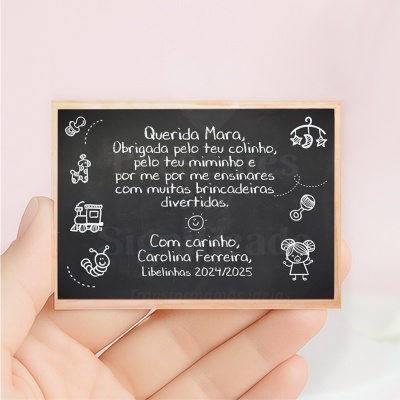 Mini quadro negro com mensagem escrita em português e desenhos infantis brancos, segurado por mão.