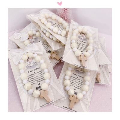 Pulseiras brancas com cruz de madeira em embalagem transparente sobre fundo rosa claro