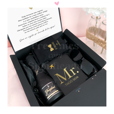 Caixa preta com garrafa, t-shirt preta com texto dourado e óculos de sol dentro