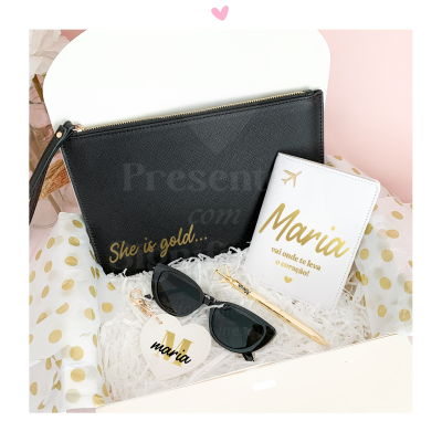 Bolsa preta, carteira de passaporte branca com texto dourado 'Maria vai onde te leva o coração!' e óculos de sol pretos sobre fundo branco com pontos dourados.