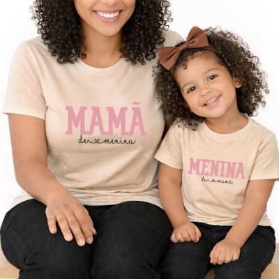 Mãe e filha com t-shirts combinando bege e texto em rosa e preto.