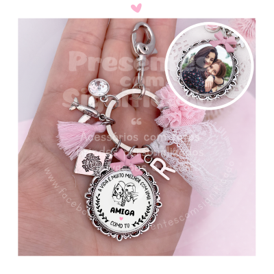 Porta-chaves metálico com pendentes rosa, branco e ilustração de amigas, segurado numa mão com fundo branco e rosa