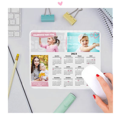 Calendário 2023 com fotos de crianças e texto 'MADRINHA MAIS FIXE', sobre mesa de escritório com acessórios