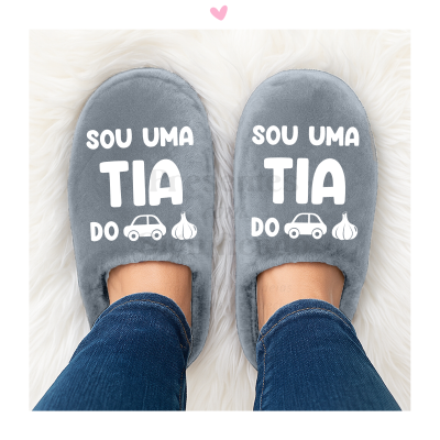 Chinelos cinza felpudos com texto branco e ícones, pés com calças de ganga sobre tapete branco