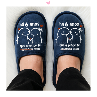 Chinelos azuis com desenho e texto em português sobre superfície branca felpuda.