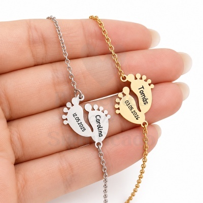 Dois colares com pendentes em forma de pés de bebé, um prateado com nome Carolina e data 12.05.2025, outro dourado com nome Tomás e data 03.05.2026