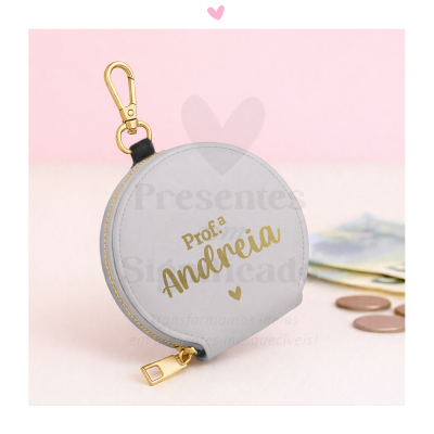 Bolsa redonda cinzenta com fecho e mosquetão dourados e texto personalizado numa superfície clara