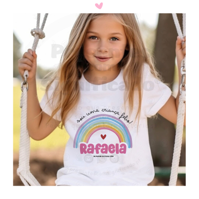 Camisola branca de criança com estampa colorida e texto, usada por menina loira no baloiço