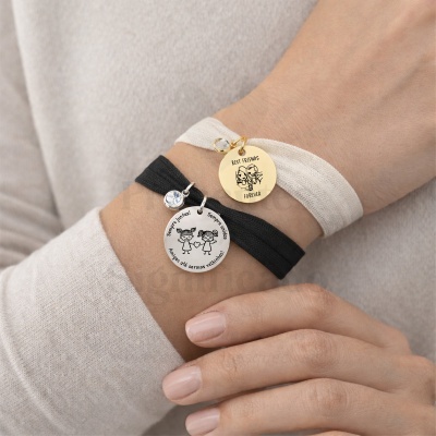 Pulseiras com pendentes metálicos e ilustrações de amigas, texto em português e inglês, em pulso de pessoa.