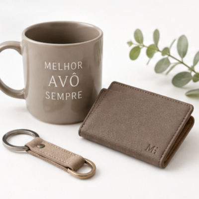 Conjunto de caneca cinza, carteira de pele castanha e porta-chaves em pele bege em fundo branco com planta decorativa