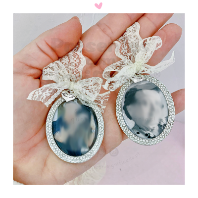 Dois mini espelhos ovais com moldura prateada e fita de renda branca em fundo claro.