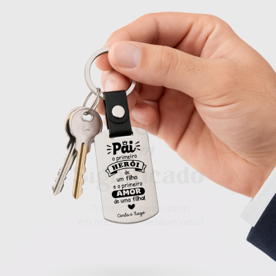 Chaveiro metálico retangular com frase em português preso a duas chaves e segurado por mão