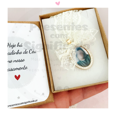 Caixa com pendente oval dourado e cartão com texto em português