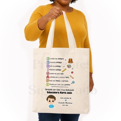 Saco de tecido bege com texto colorido e ilustrações pequenas, segurado por pessoa com camisola amarela.