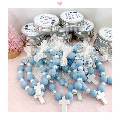 Pulseiras de contas azuis com cruzes brancas e latas metálicas com etiquetas, sobre fundo rosa com textura
