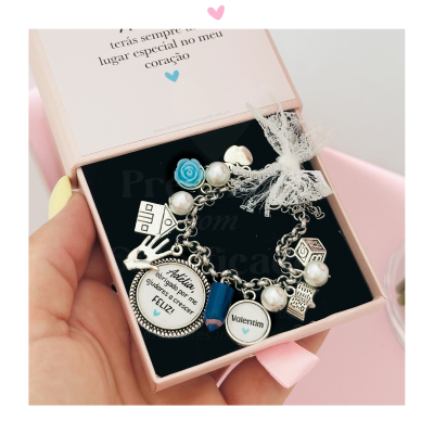 Pulseira prateada com pendentes diversos numa caixa rosa
