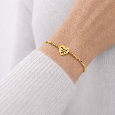 Pulseira dourada com pendente coração gravado usada no pulso