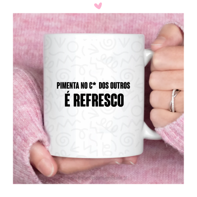 Caneca branca em cerâmica com texto humorístico em preto e padrões cinzentos, segurada por mãos com suéter rosa.