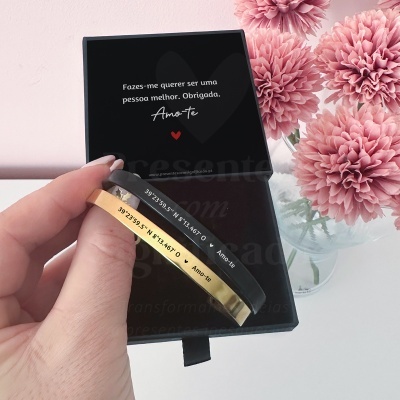 Pulseiras dourada e preta com gravação em caixa preta com mensagem e flores cor-de-rosa ao lado